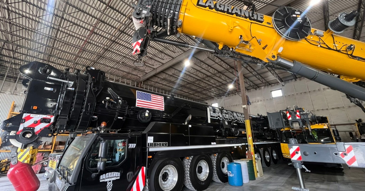 A truck crane with a telescopic boom raised above a long black all-terrain crane with its crane lowered.