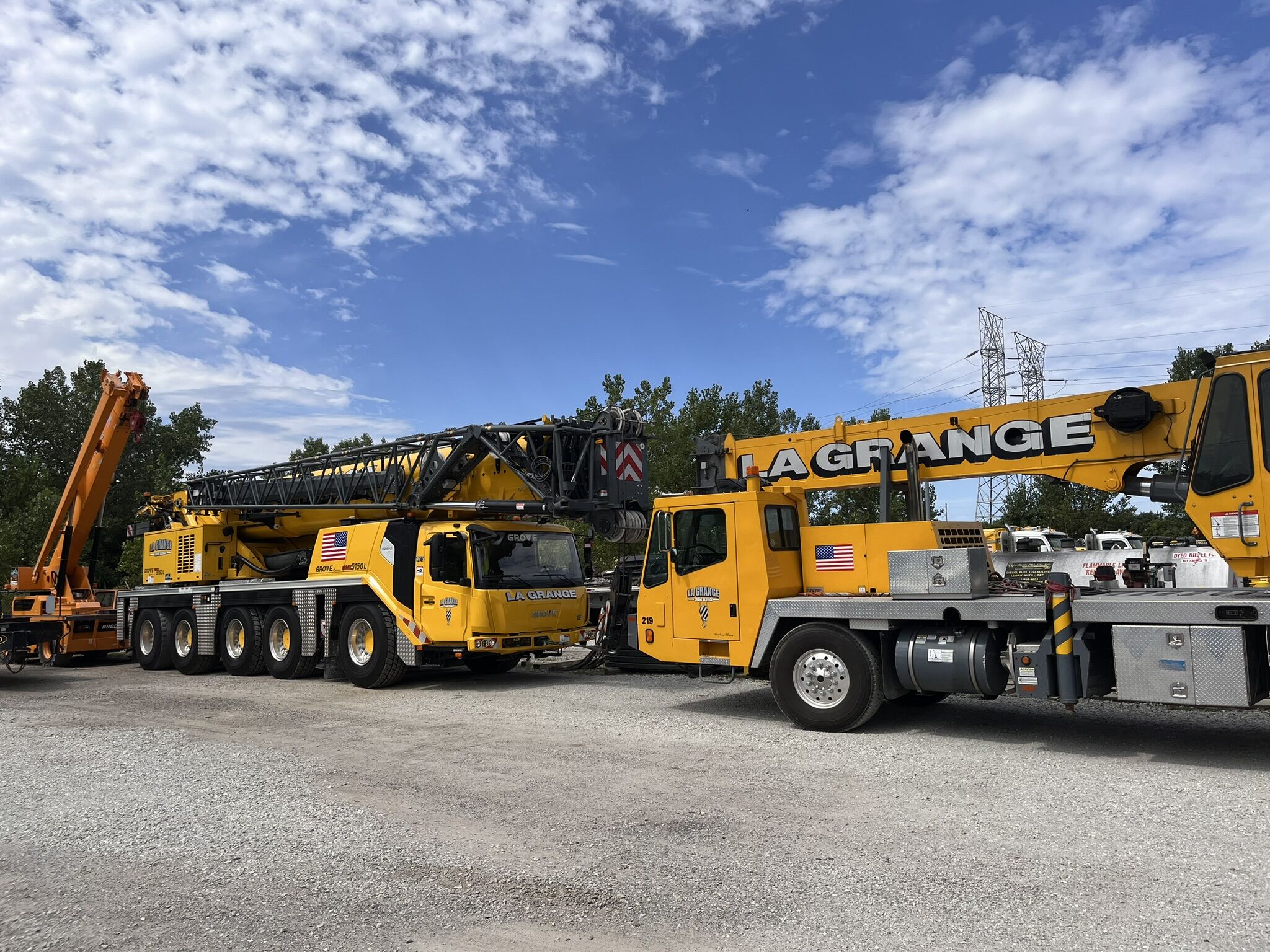 Two yellow all-terrain cranes outside during the daytime. Both cranes sit in front of each other with their booms down.