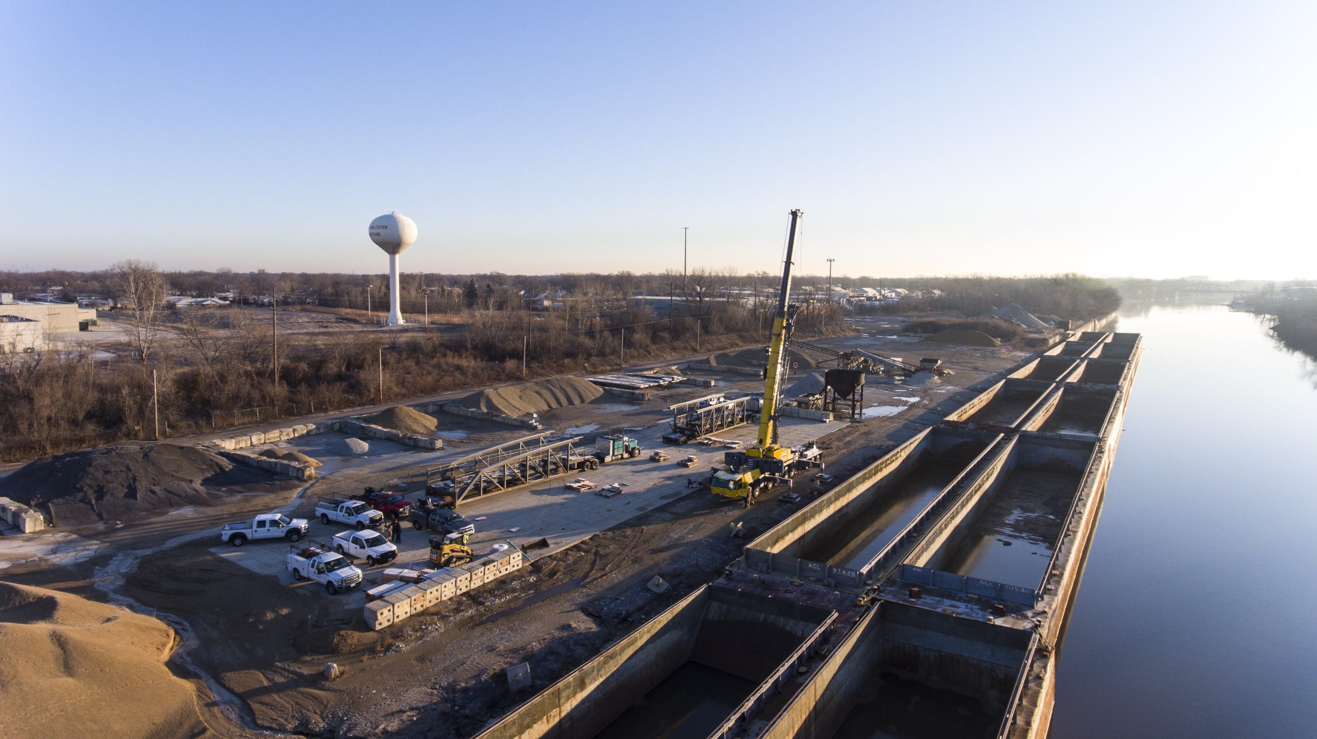 A construction site on a sunny day. A yellow crane is parked on the construction site with its arm extended in the air.