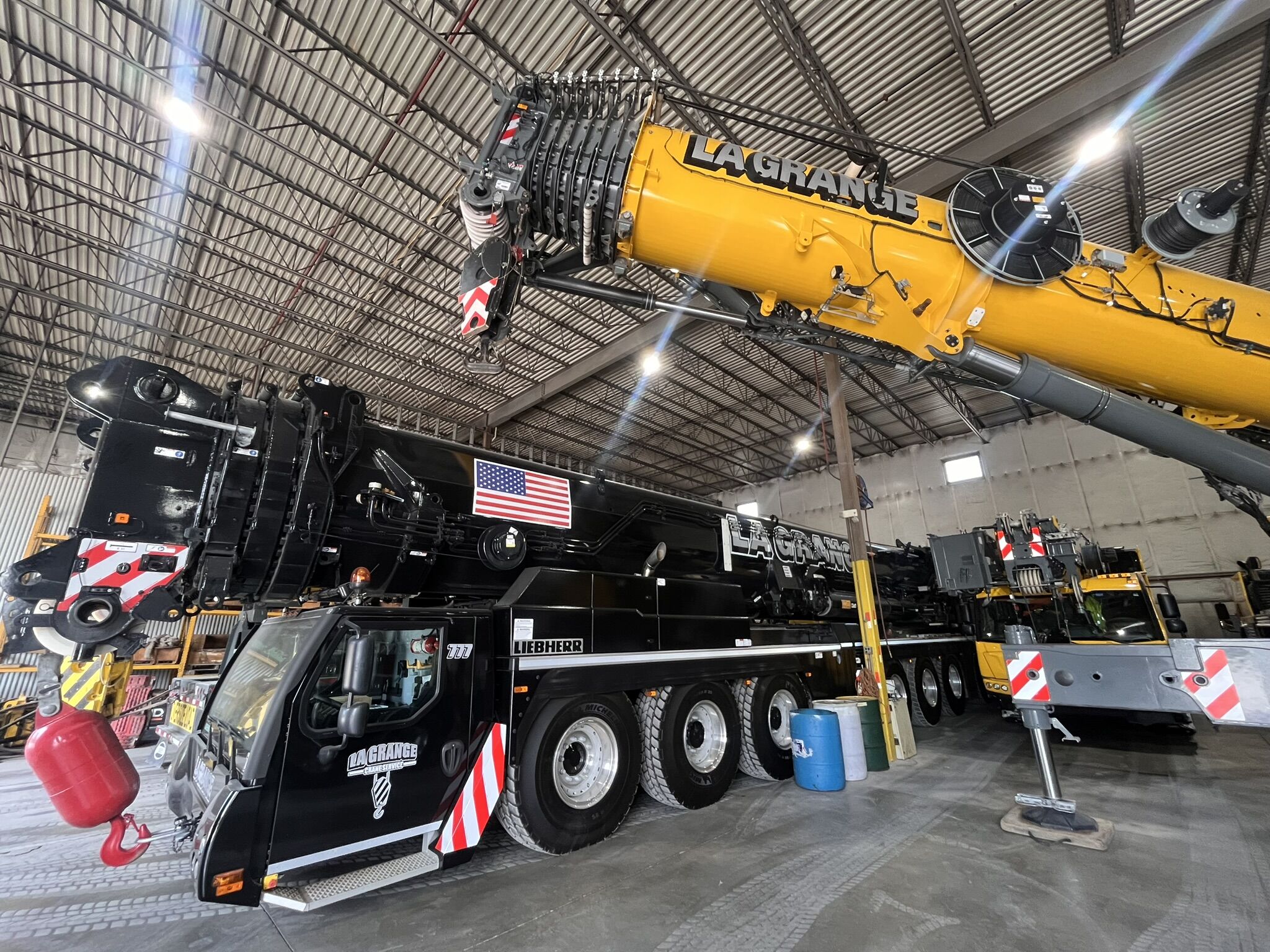 A long, black telehandler parked inside a large garage. The vehicle sits next to a yellow telehandler.