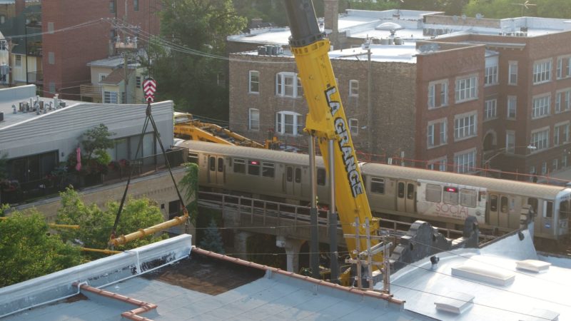 A yellow telehandler with its boom arm extended into the air next to a train. "La Grange" is printed on the crane arm.